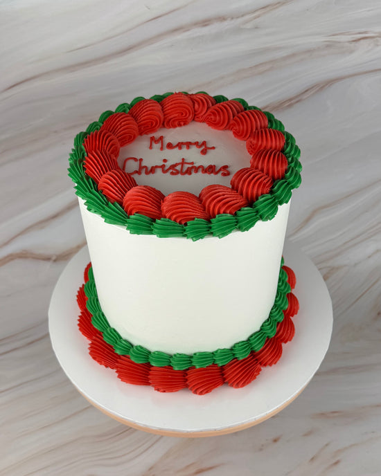 White cake with red and green piping (top view). Writing on cake says Merry Christmas.